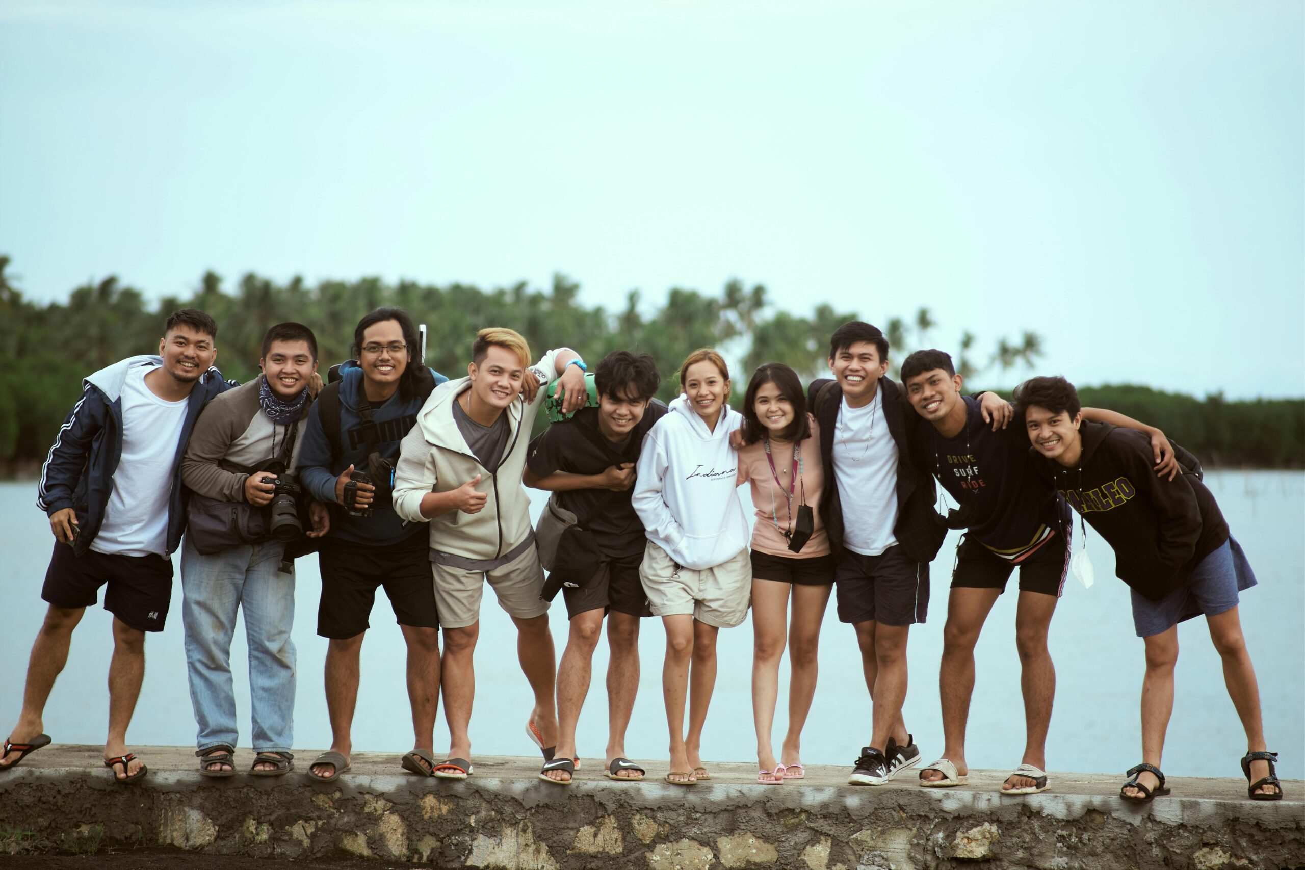 Cheerful group of friends posing by a lakeside, enjoying a warm day outdoors.